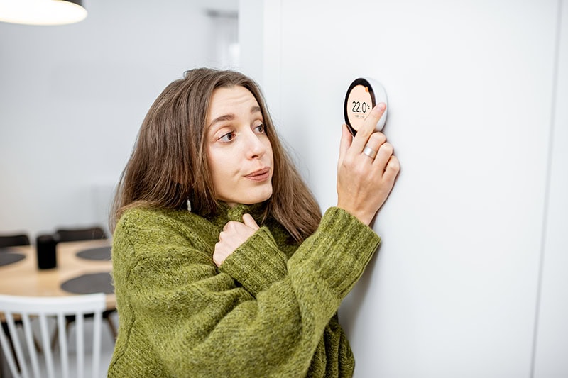 Why Is My Heat Pump Turning On and Off Frequently? A lady turning up her thermostat.